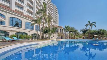 A hotel with a swimming pool, palm trees, and a multi-story building.