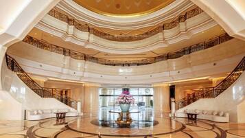 A grand hotel lobby with a central fountain, multiple staircases, and a spacious marble floor.