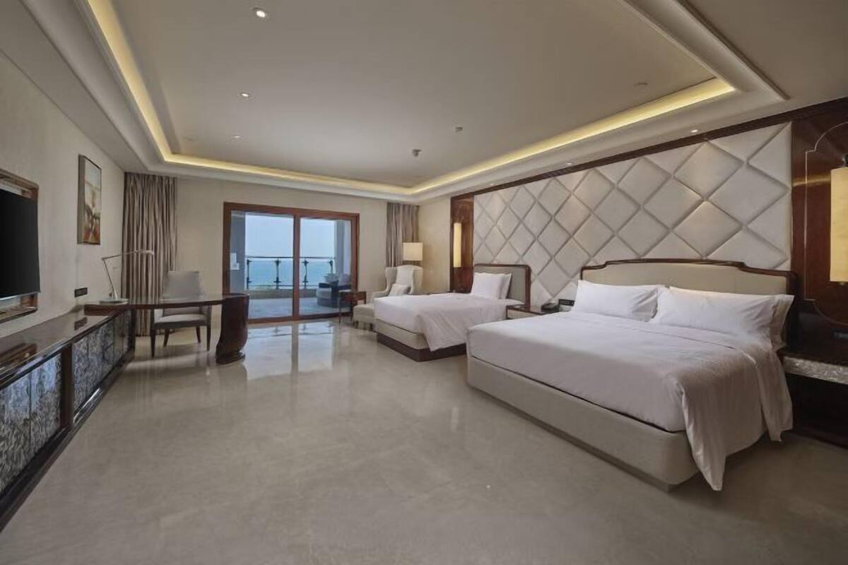 A hotel room with two beds, a desk, a TV, and a balcony with a view.