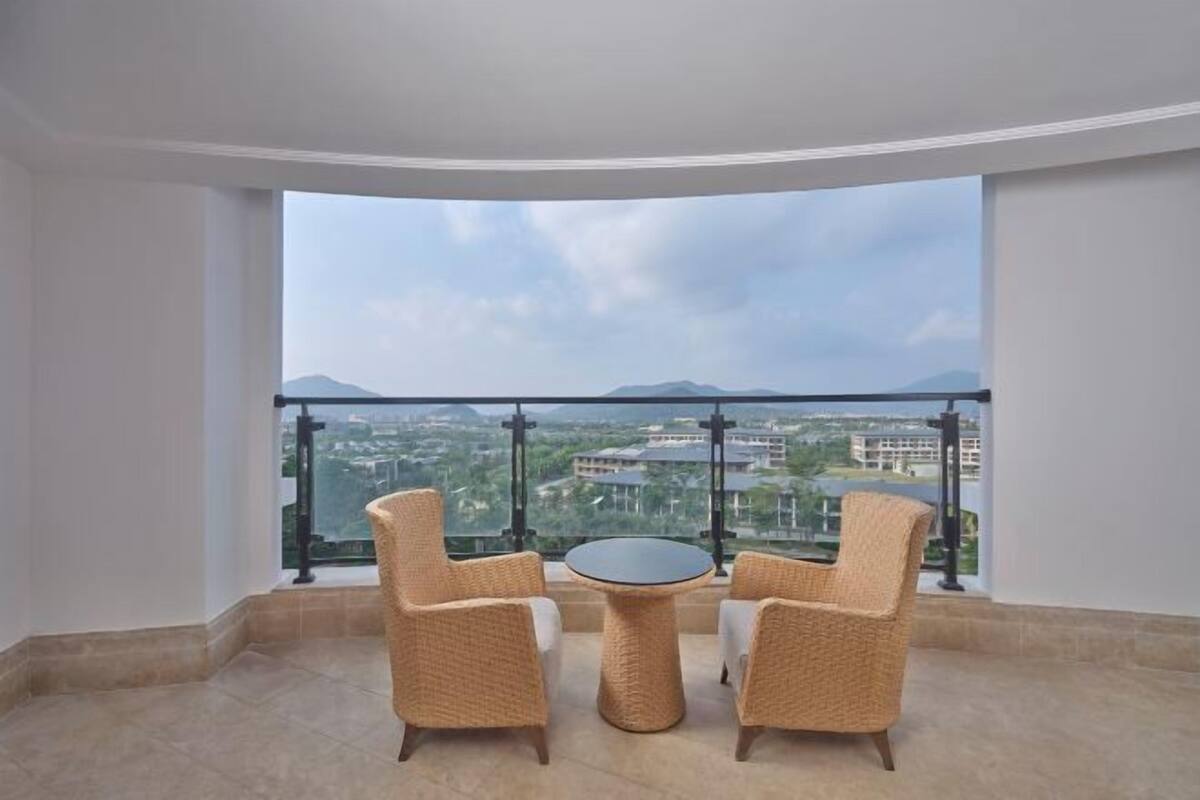 A balcony with wicker chairs and a small table, offering a view of a cityscape and mountains.