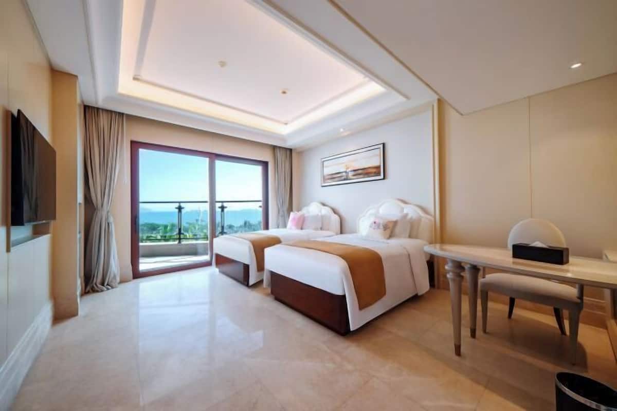 A hotel room with two beds, a desk, a TV, and a balcony with a view.