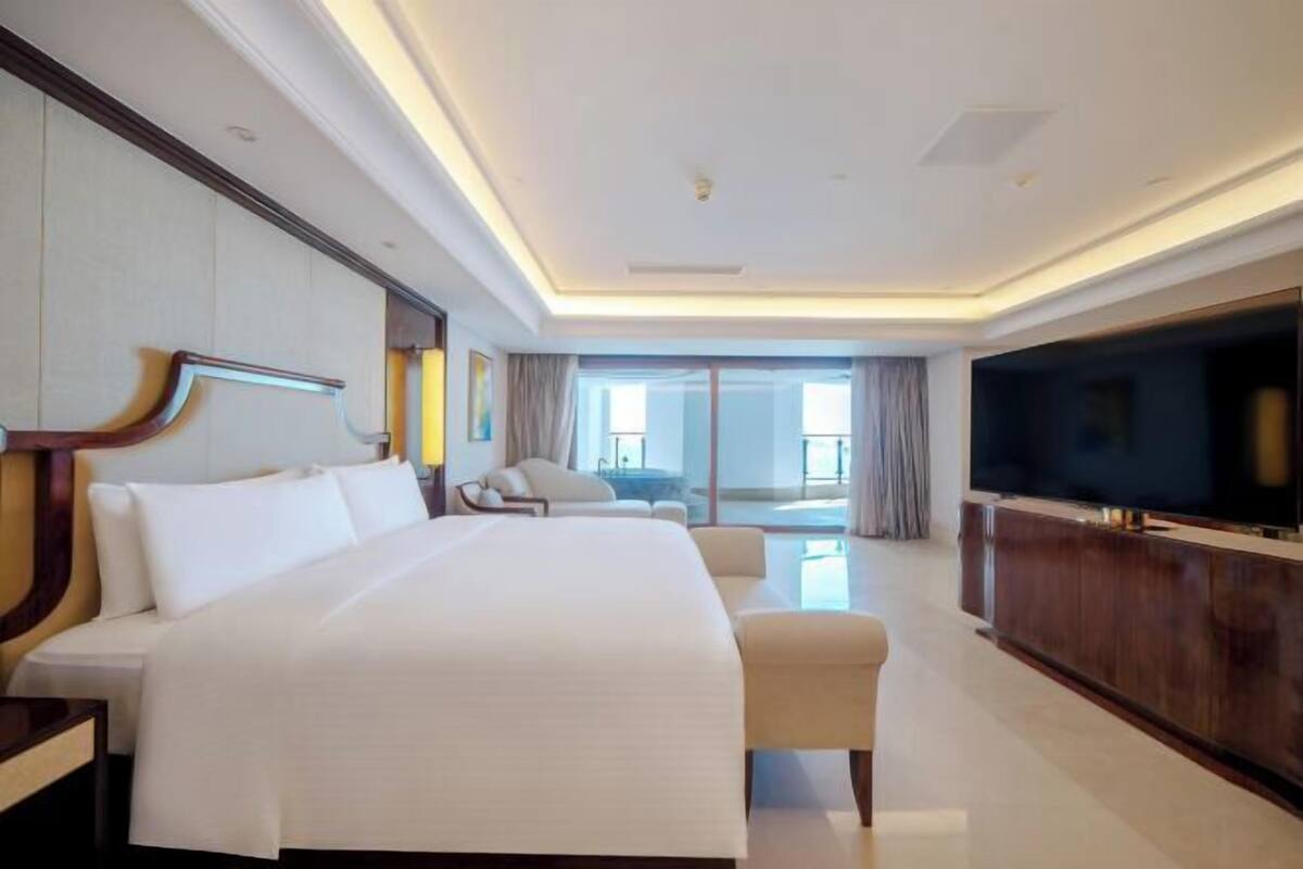 A hotel room with a large bed, a television, a seating area, and a view of the outdoors.