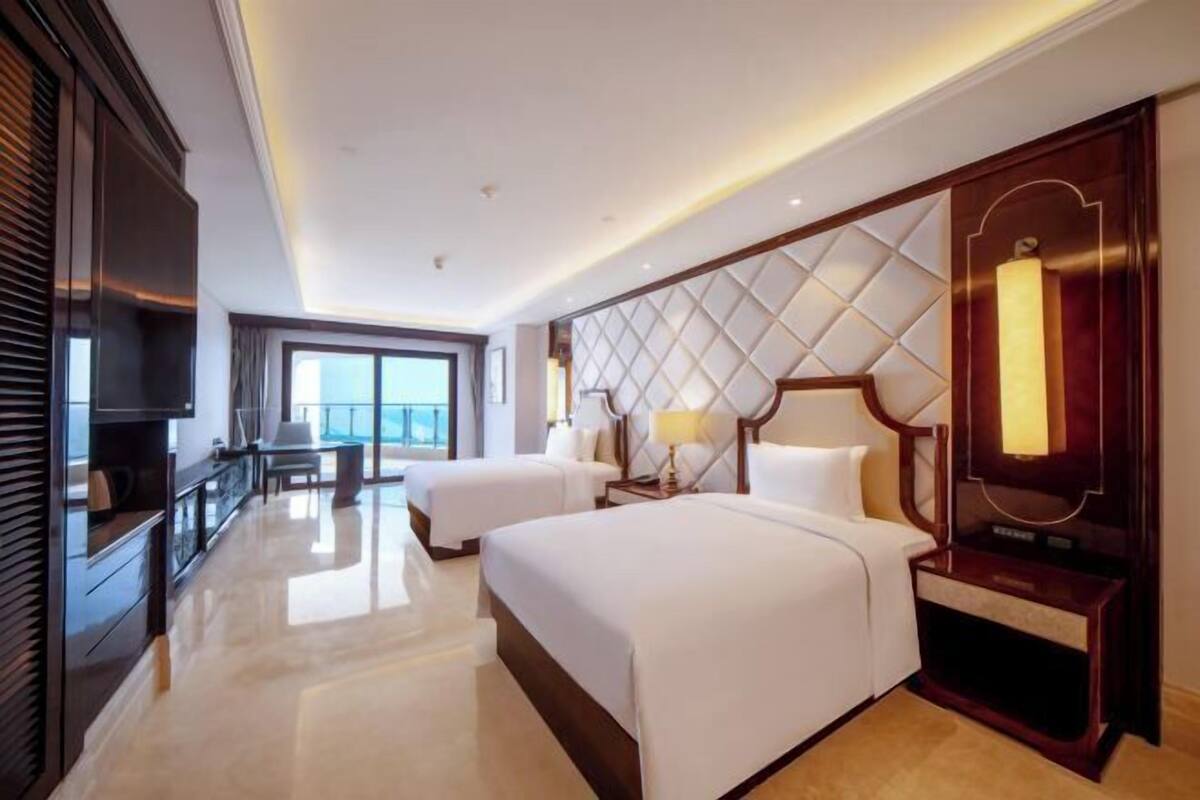 A hotel room with two beds, a TV, a desk, and a large window.