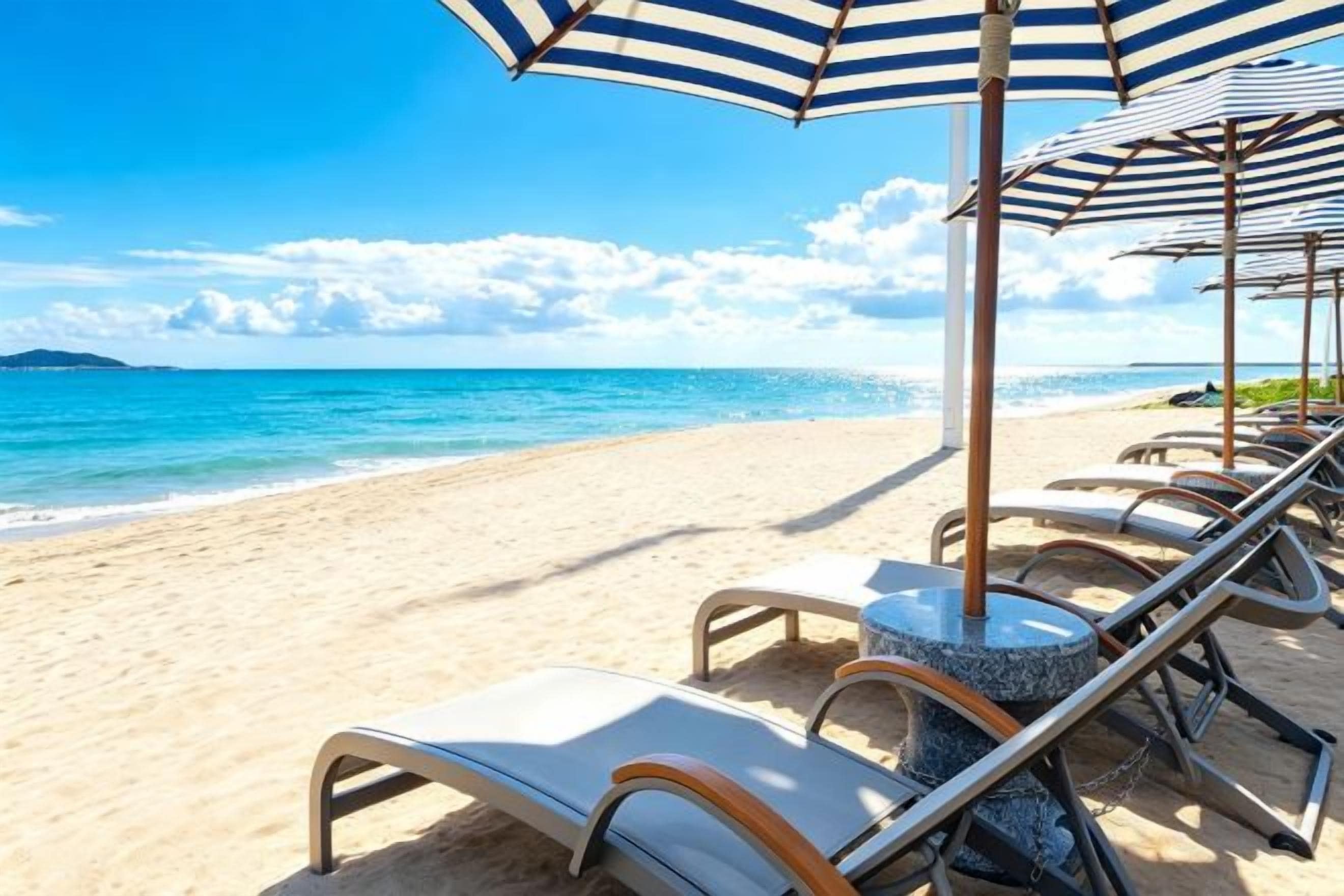 A beach with lounge chairs and umbrellas, a clear sky, and the ocean.