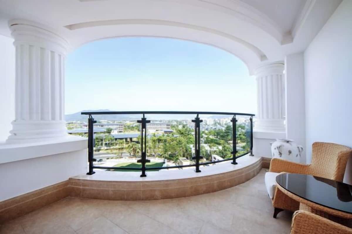 A balcony with a curved railing, a wicker chair, a small table, and a view of a cityscape.