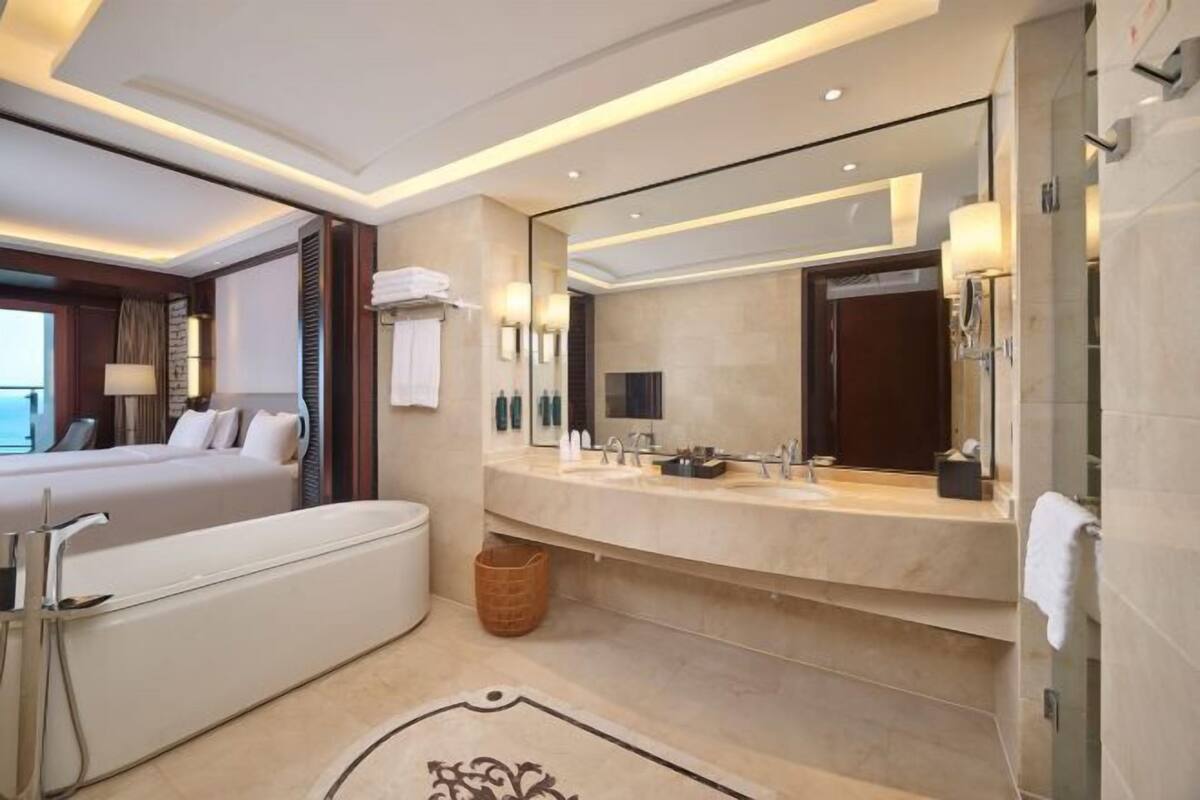 A modern hotel bathroom with a large bathtub, a double sink vanity, and a large mirror.