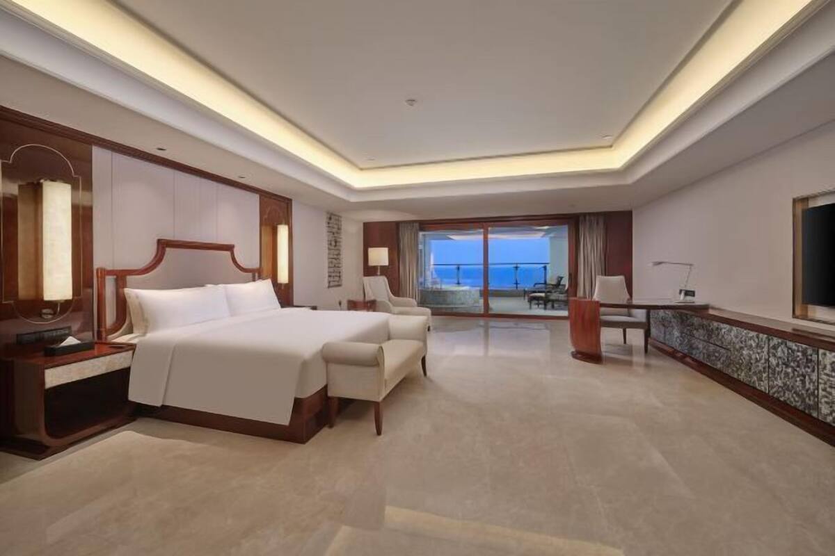 A hotel room with a large bed, a desk, a chair, and a view of the sea.