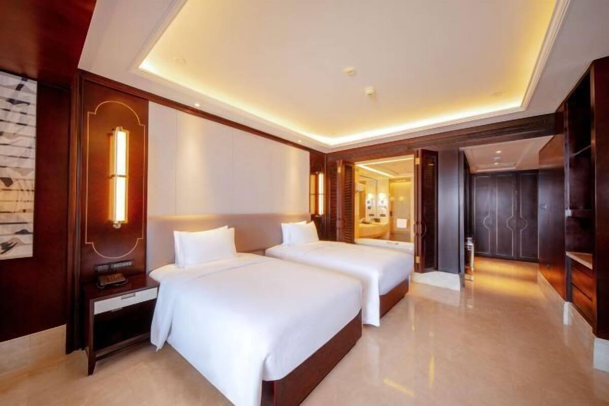 A hotel room with two beds, a nightstand, a mirror, and a door leading to another room.