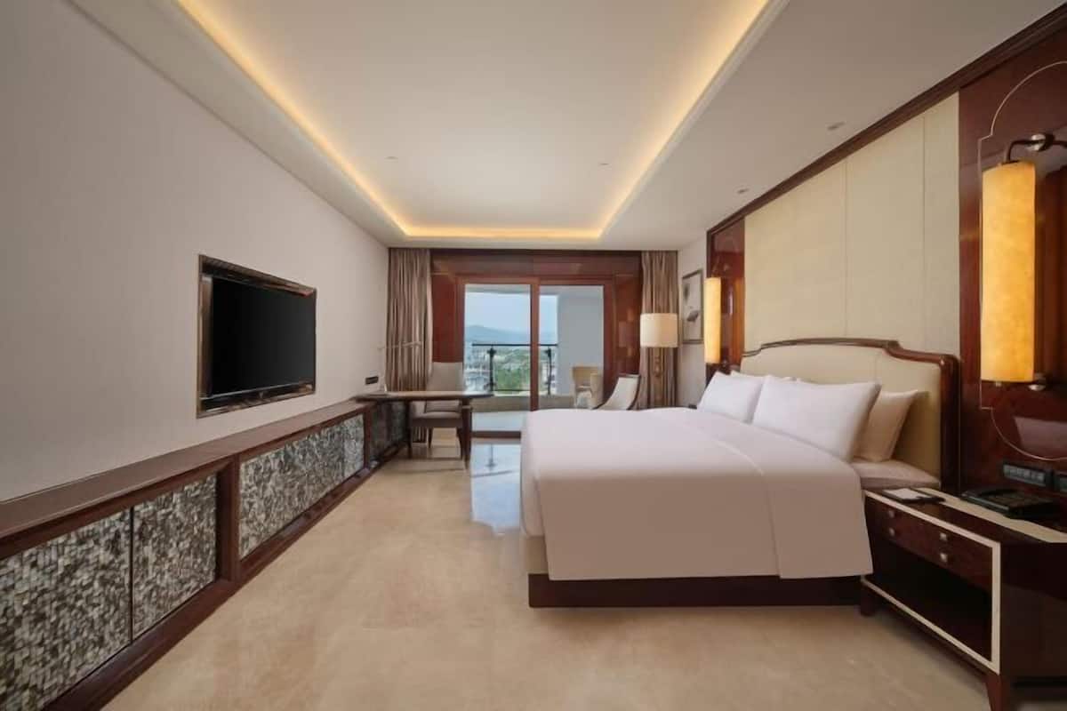 A hotel room with a large bed, a desk, a flat-screen TV, and a balcony with a view.