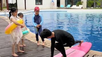 A swimming pool area with a wooden deck, a pink float, and a person in a wetsuit.