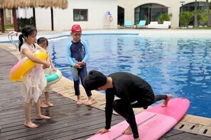 A swimming pool area with a wooden deck, a pink float, and a person in a wetsuit. - DoubleTree by Hilton Sanya Bay (Sanya)