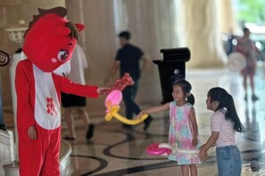 Um mascote com fantasia vermelha interagindo com crianças em um saguão.