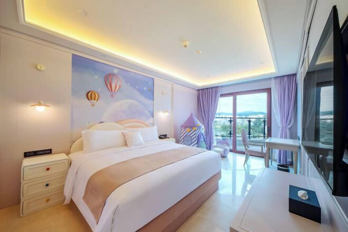 A modern hotel room with a large bed, a desk, a balcony with a view, and a wall mural.