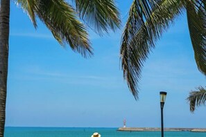 A beach scene with palm trees, a clear blue sky, and a distant lighthouse. - DoubleTree by Hilton Sanya Bay (Sanya)