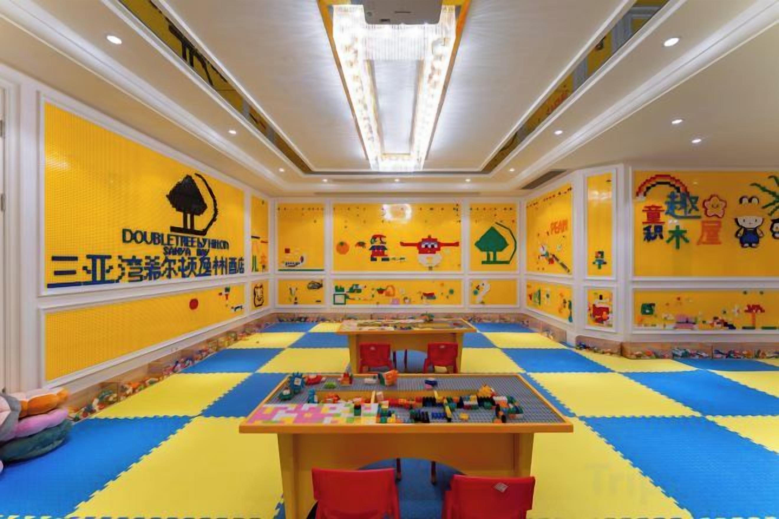 Una sala de jocs amb estores de colors, una taula de jocs i decoracions de LEGO a la paret.