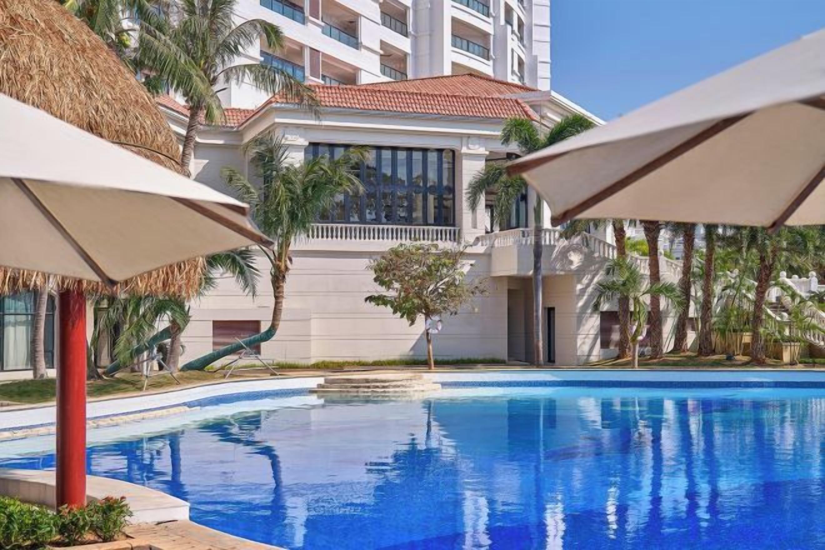 Une piscine dotée de parasols, de palmiers et d’un bâtiment avec des balcons.