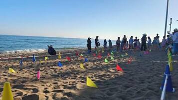 A beach with people and colorful flags on the sand.