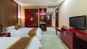 Ein Hotelzimmer mit zwei Betten, einem Fernseher, einem Schreibtisch und einem Kleiderschrank.