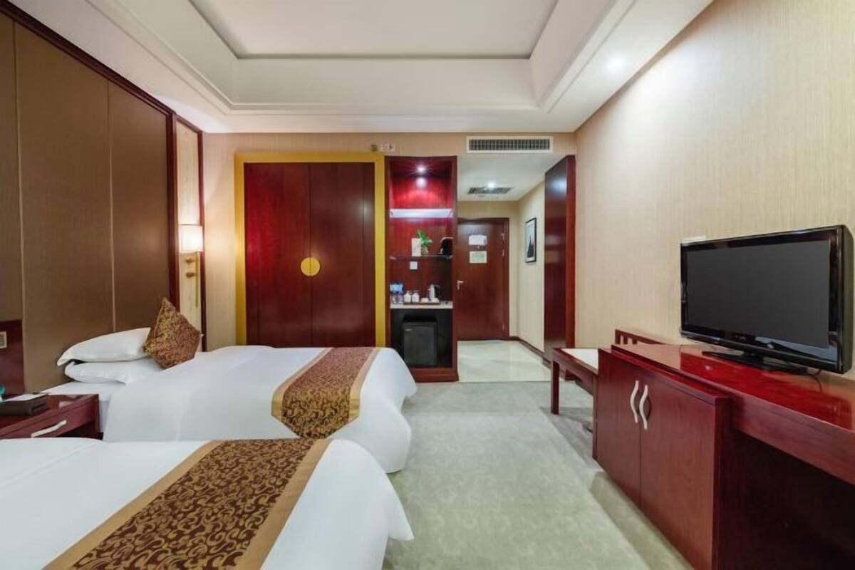 Ein Hotelzimmer mit zwei Betten, einem Fernseher, einem Schreibtisch und einem Kleiderschrank.