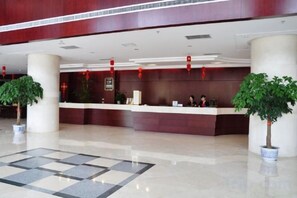 Zona de recepción de un hotel con suelo de mármol, mostrador de recepción y dos plantas en macetas.