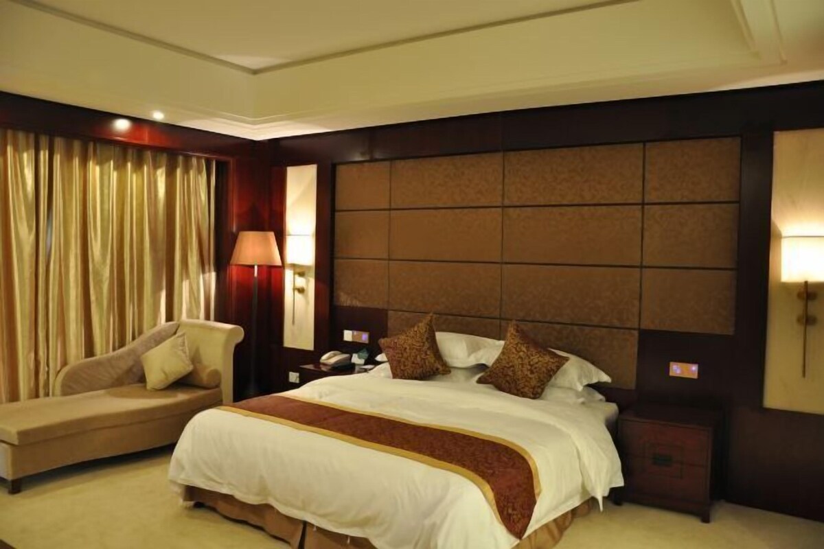 A hotel room with a large bed, a sofa, a nightstand, and a lamp.
