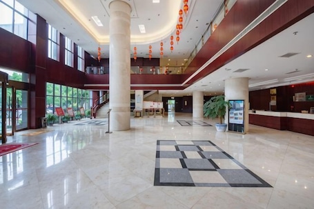 A spacious lobby with a checkered floor, large windows, and a reception desk.. Qihong International Hotel