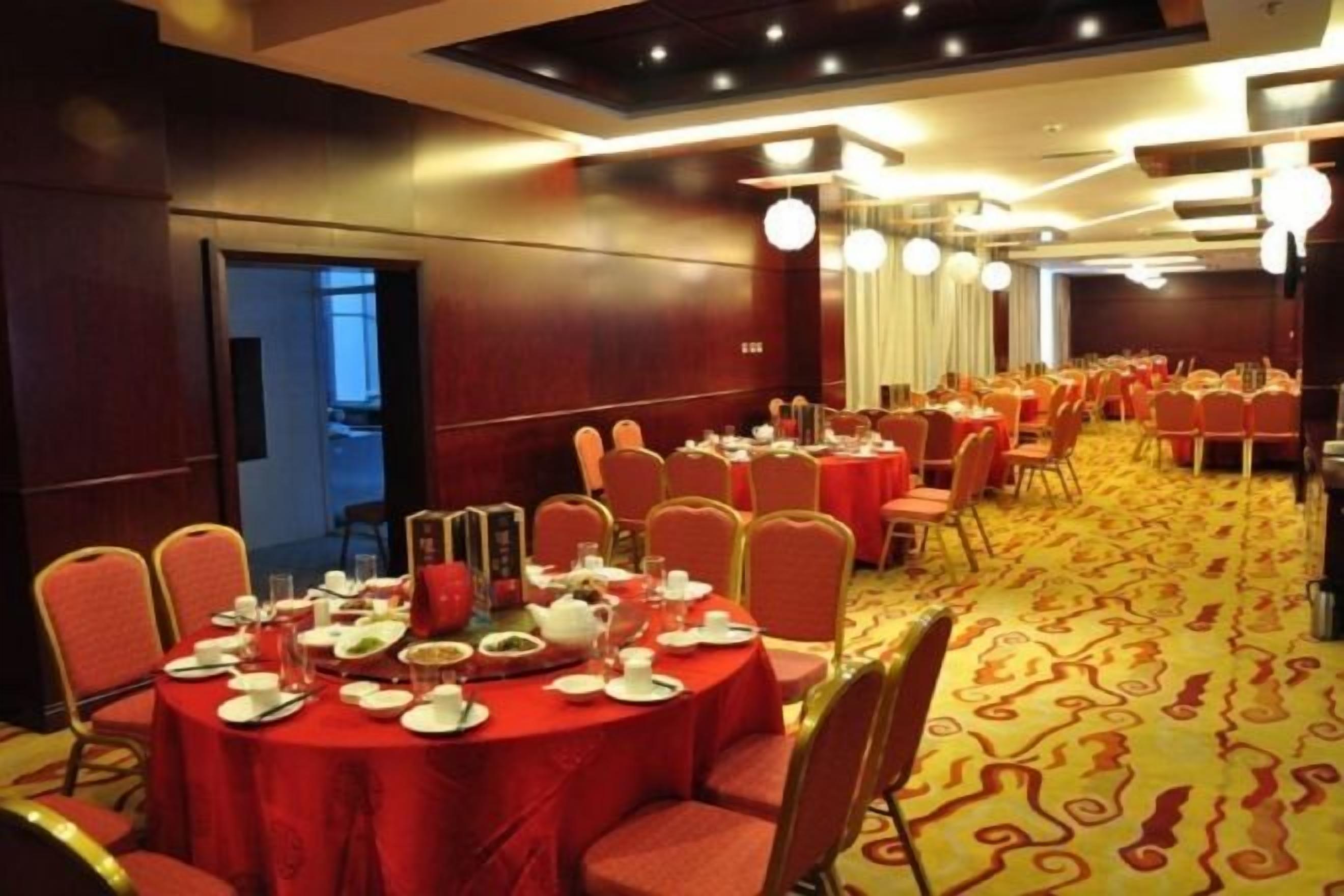 Sala de conferências com mesas redondas, cadeiras e piso coberto por carpete.