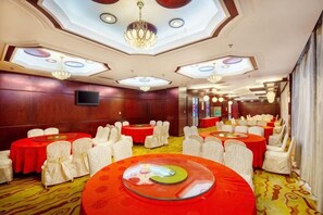 Un salón de banquetes con mesas redondas, sillas blancas y una mesa central de vidrio.