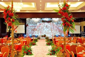 Une salle de banquet avec des tables rondes, des centres de table floraux et une scène équipée d’un écran de projection.