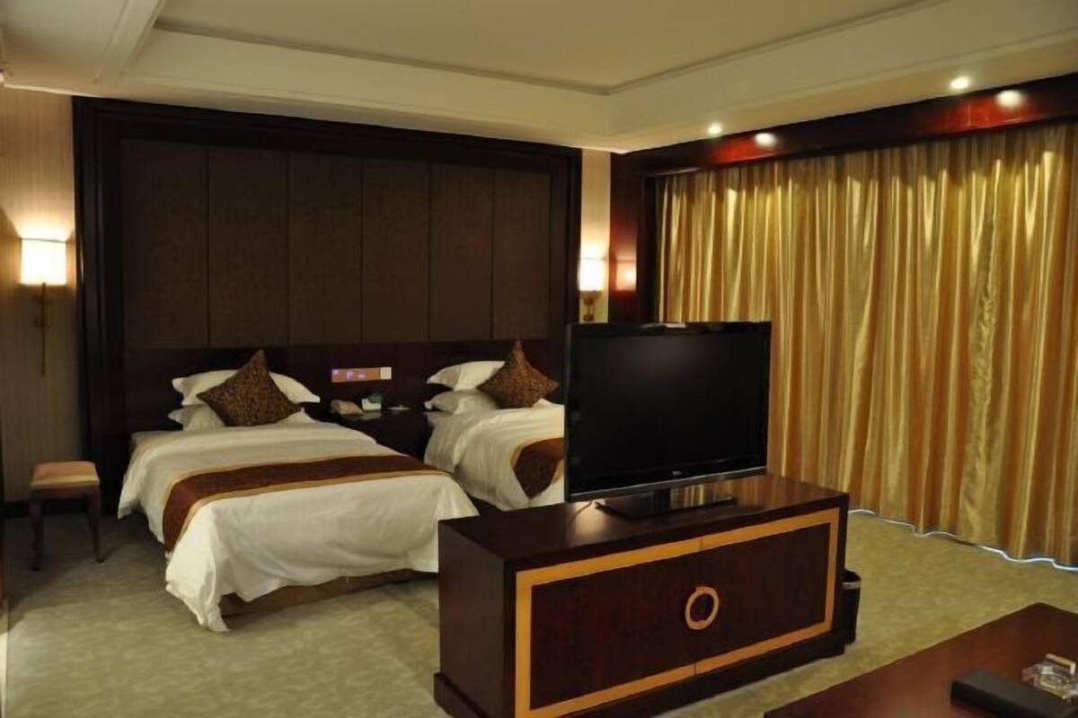 Ein Hotelzimmer mit zwei Betten, einem Flachbildfernseher, einem Holzschrank und einem großen Fenster mit Vorhängen.