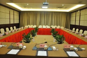 A conference room with a long table, chairs, nameplates, microphones, and a projector screen. - Qihong International Hotel (Qimen)