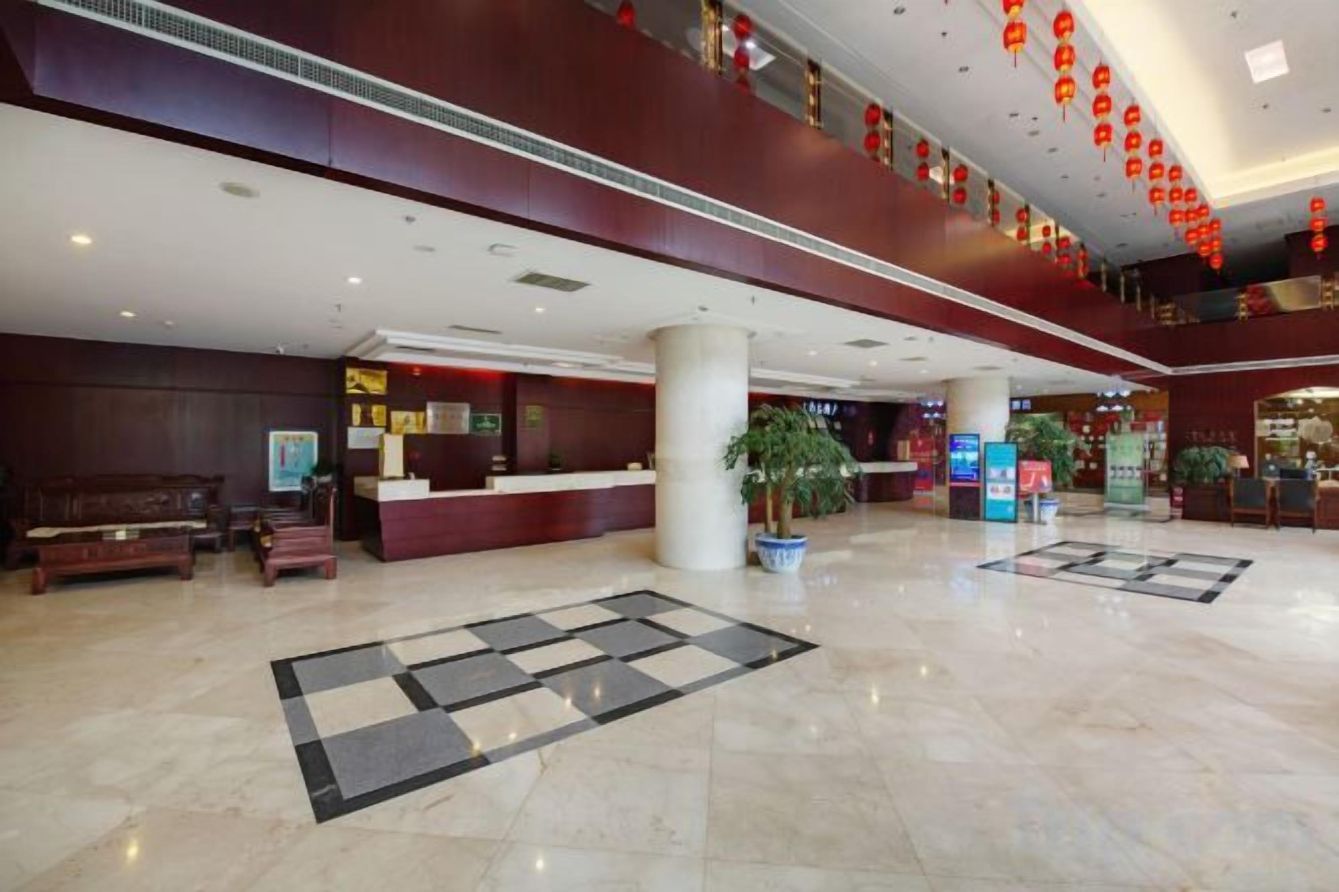 A hotel lobby with a reception desk, seating area, and decorative plants.