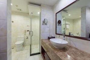 Ein modernes Badezimmer mit einer gläsernen Duschkabine, einer weißen Toilette und einem großen Spiegel über einer Marmorplatte mit einem Aufsatzbecken.