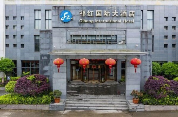 Qihong International Hotel features a modern architectural design with a symmetrical facade, flanked by large potted plants and a glass entrance.