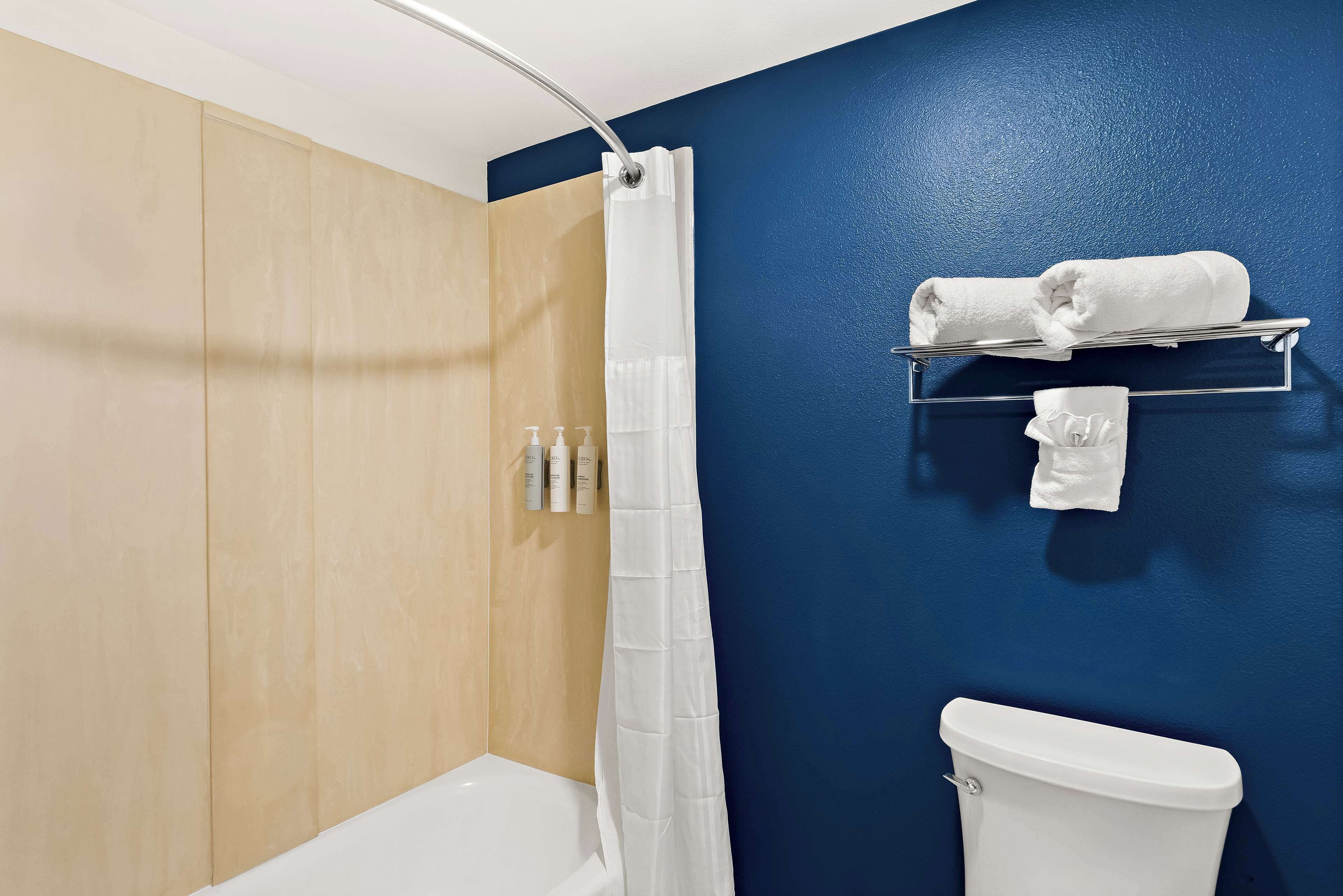 A bathroom with a white bathtub, a shower curtain, a toilet, and a towel rack with towels.