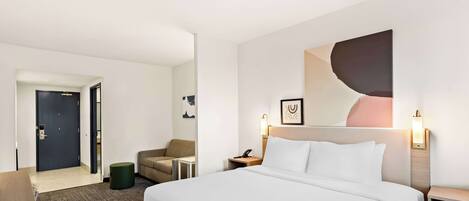 A hotel room with a large bed, a desk, a chair, a small table, and a door.