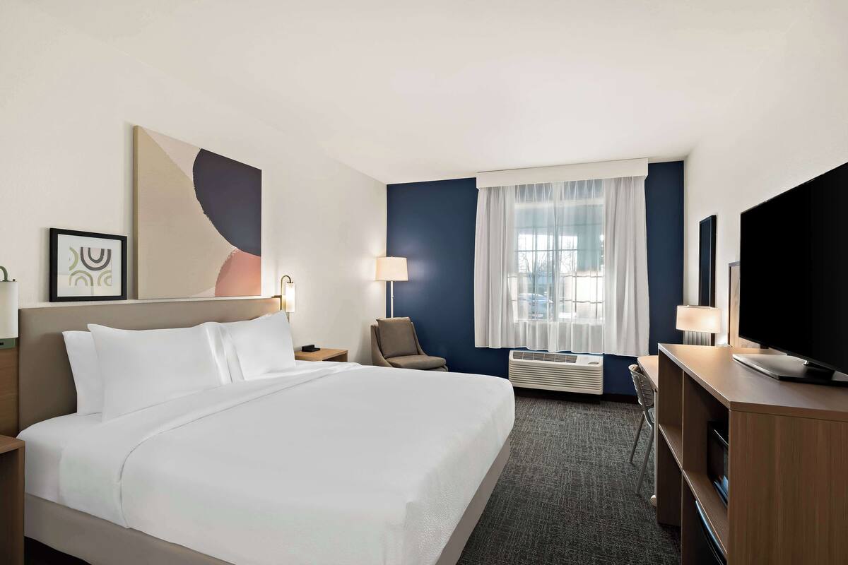 A hotel room with a large bed, a desk, a chair, a TV, and a window with curtains.