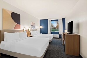 A hotel room with two beds, a desk, a TV, and a window with curtains.
