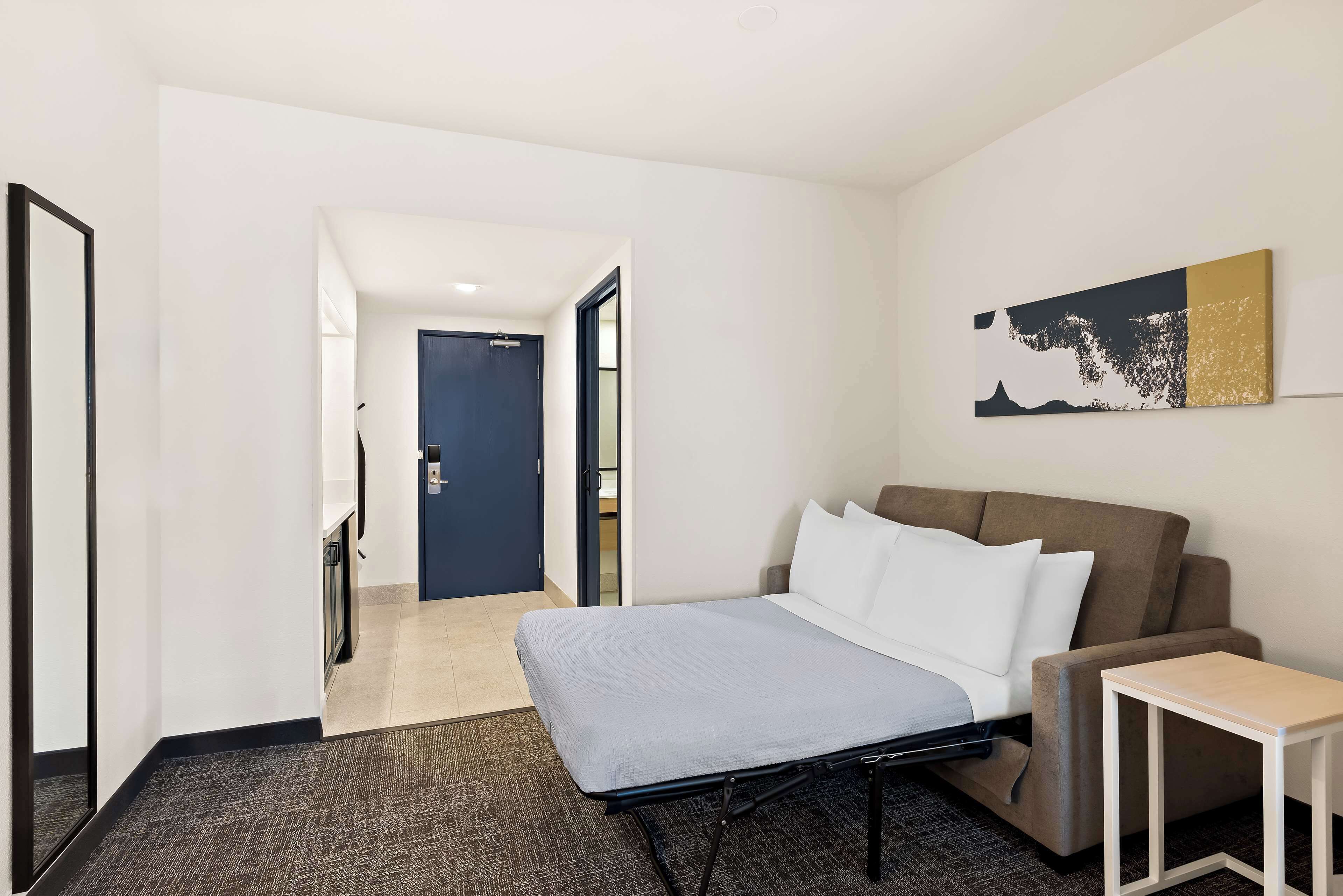 Una habitación de hotel moderna con una cama, un sofá, una mesita y un cuadro en la pared.