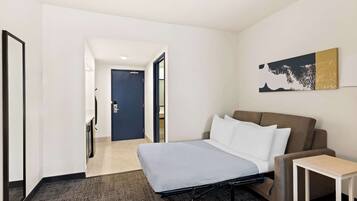 Una habitación de hotel moderna con una cama, un sofá, una mesita y un cuadro en la pared.