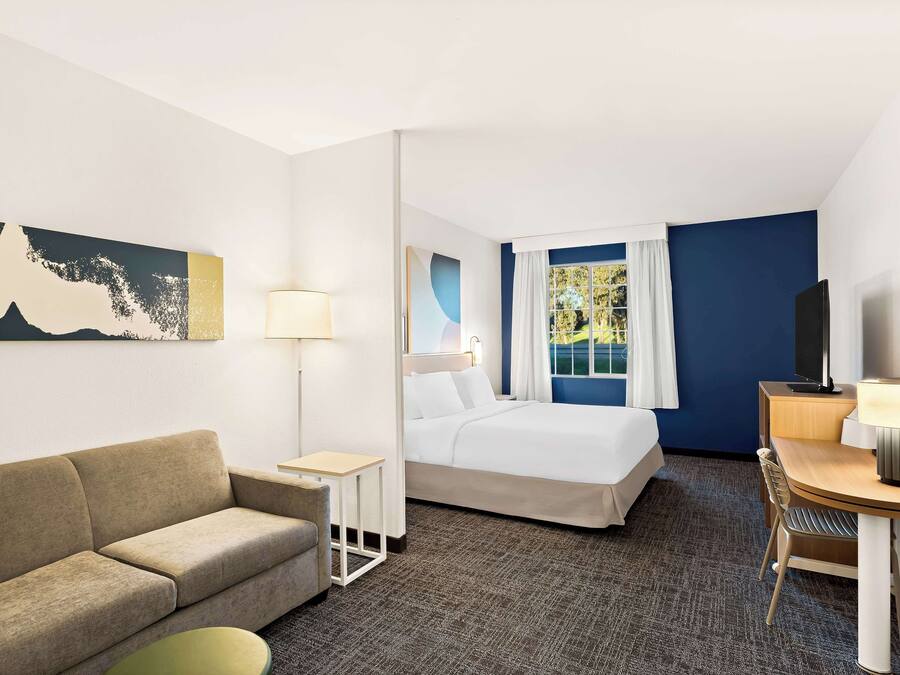 A hotel room with a bed, a sofa, a desk, a chair, a TV, and a window with curtains.