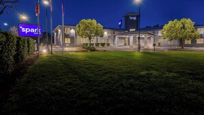A hotel with a modern design, featuring a prominent 'Spark by Hilton' sign, multiple flagpoles, and well-lit surroundings. - Spark by Hilton Williams (Williams)