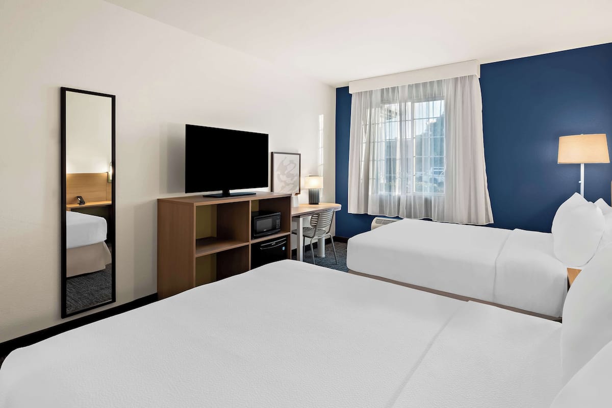 A hotel room with two beds, a TV, a desk with a chair, and a window with curtains.