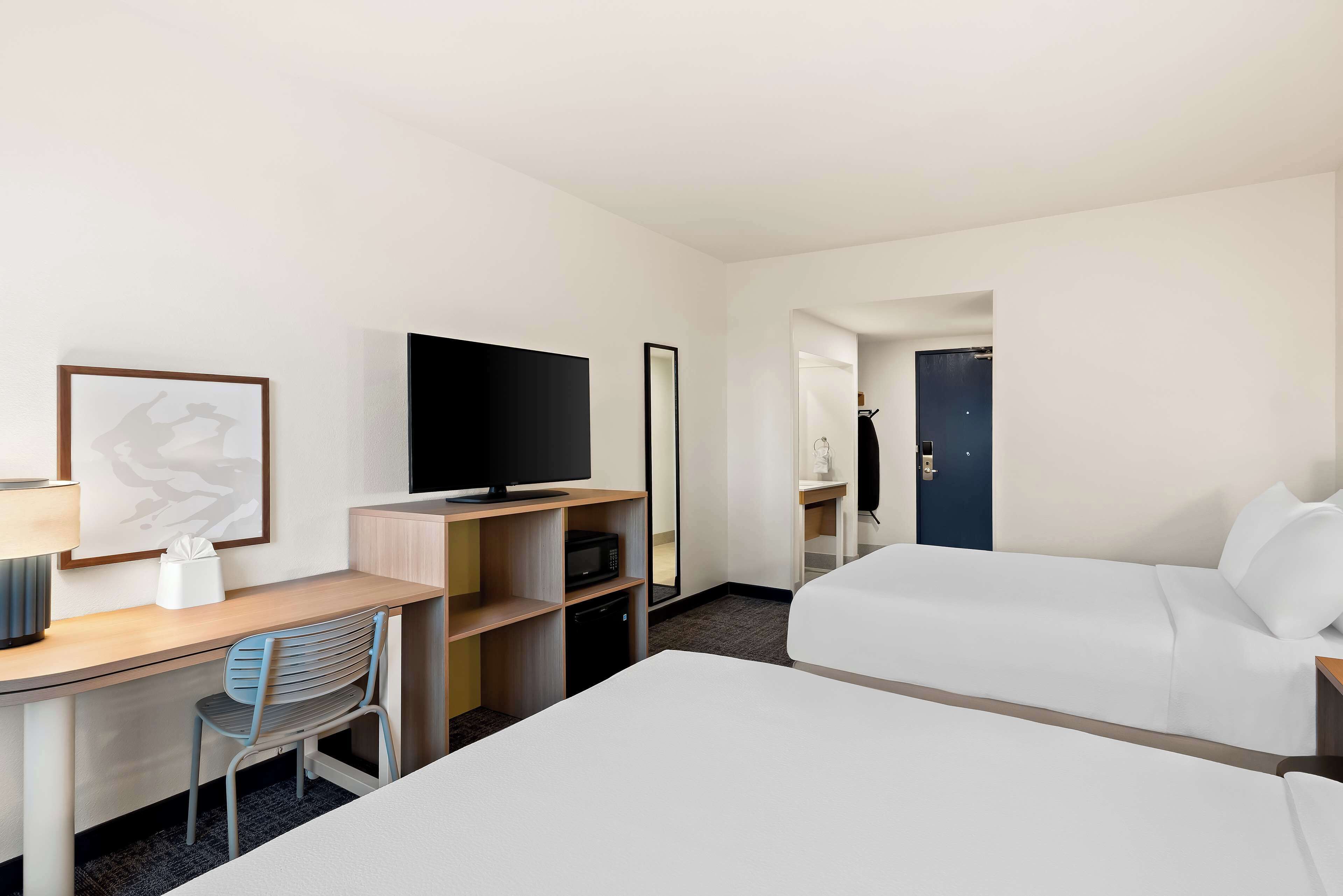 Una habitación de hotel con cama, escritorio, silla, televisor, microondas y espejo.