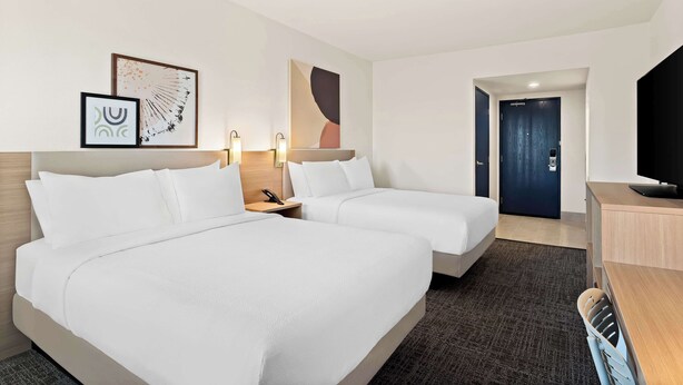 A hotel room with two beds, a desk, a TV, and artwork on the wall. - Spark by Hilton Williams (Williams)