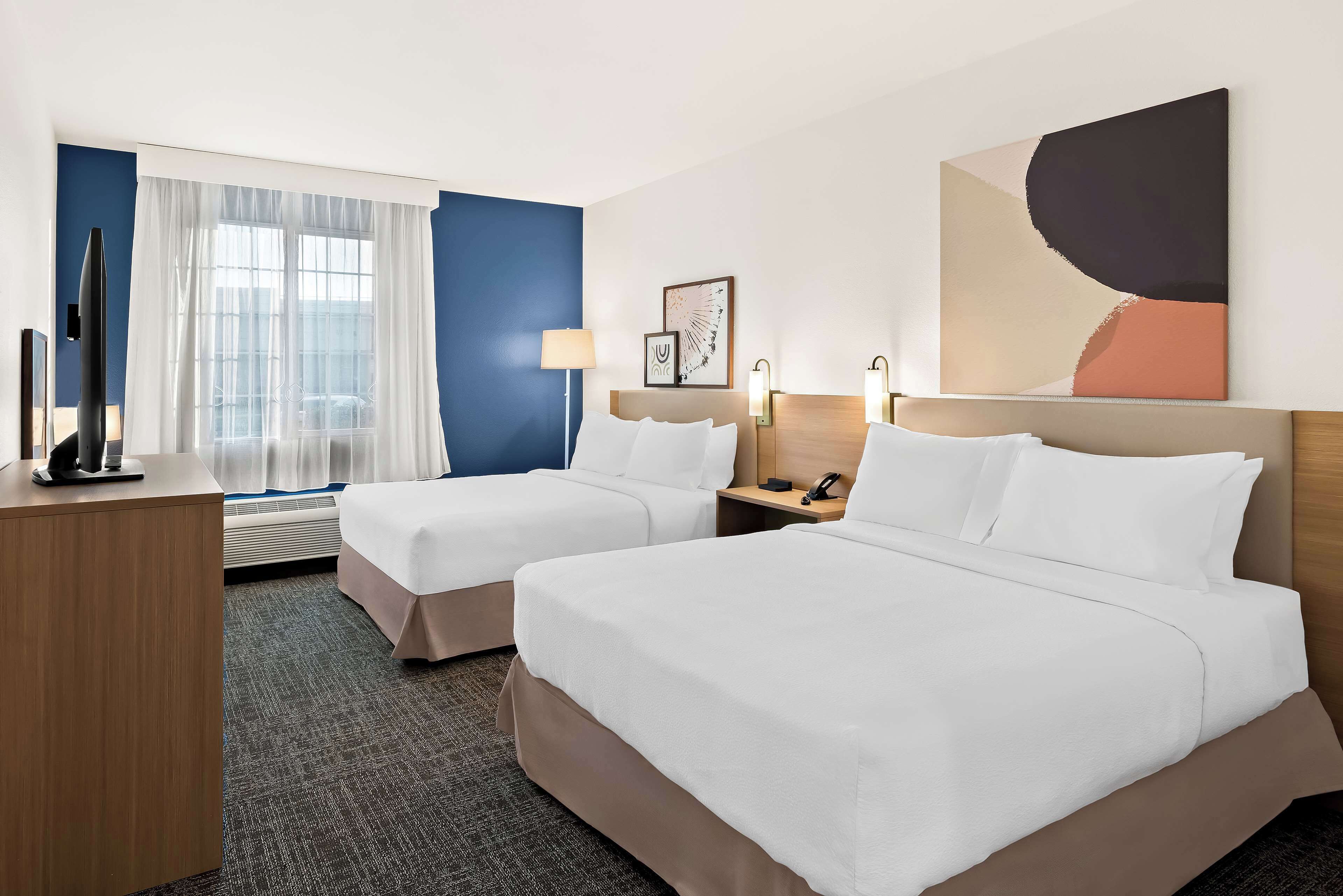 A hotel room with two beds, a desk, a TV, and a window with curtains.