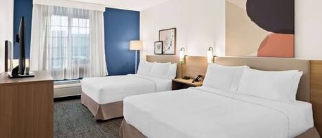 A hotel room with two beds, a desk, a TV, and a window with curtains.