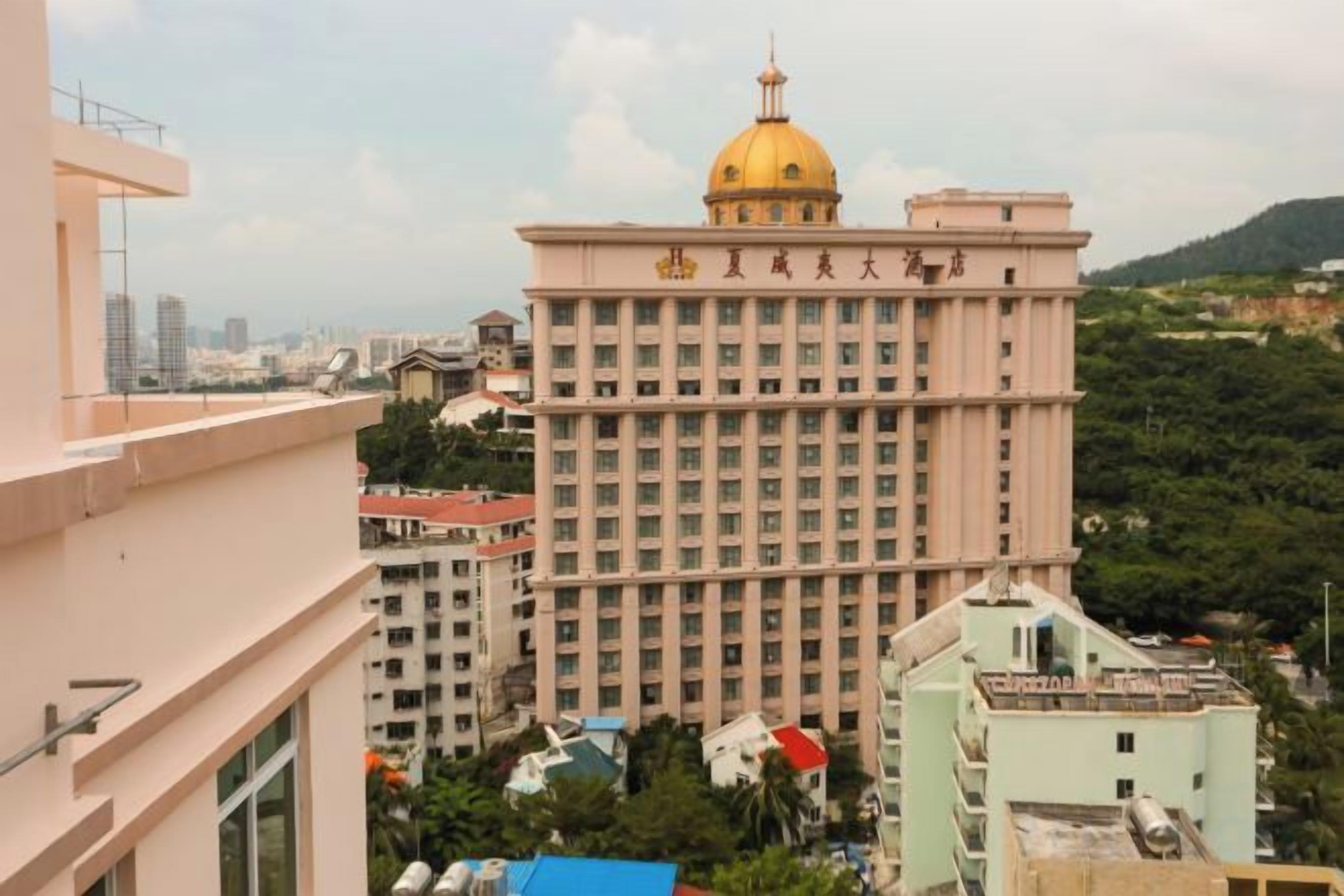 A multi-story building with a prominent golden dome, surrounded by other buildings and greenery.