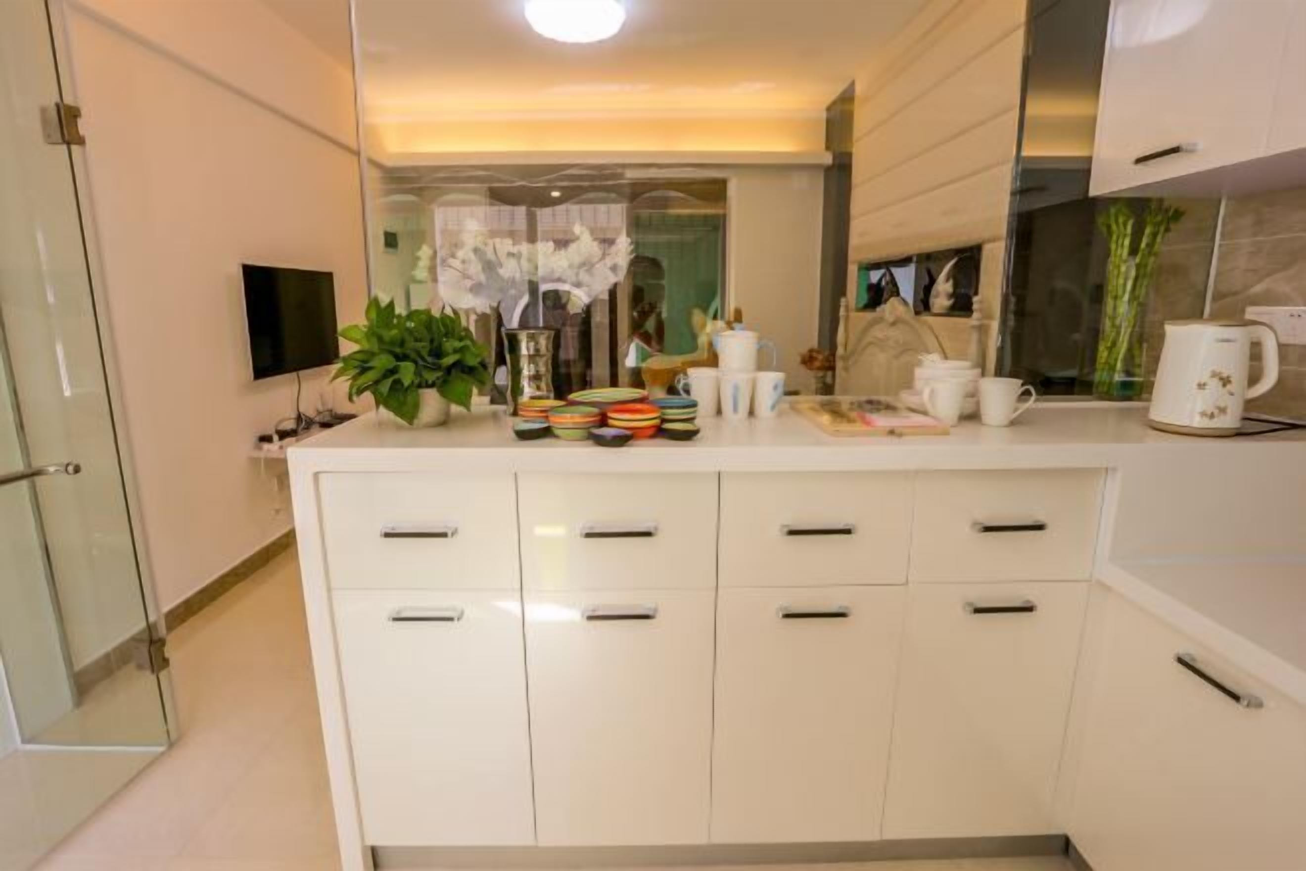 Una cocina moderna con armarios blancos, un televisor de pantalla plana, una planta en maceta y diversos utensilios de cocina sobre la encimera.