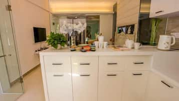 A modern kitchen with white cabinets, a flat-screen TV, a potted plant, and various kitchen items on the counter.